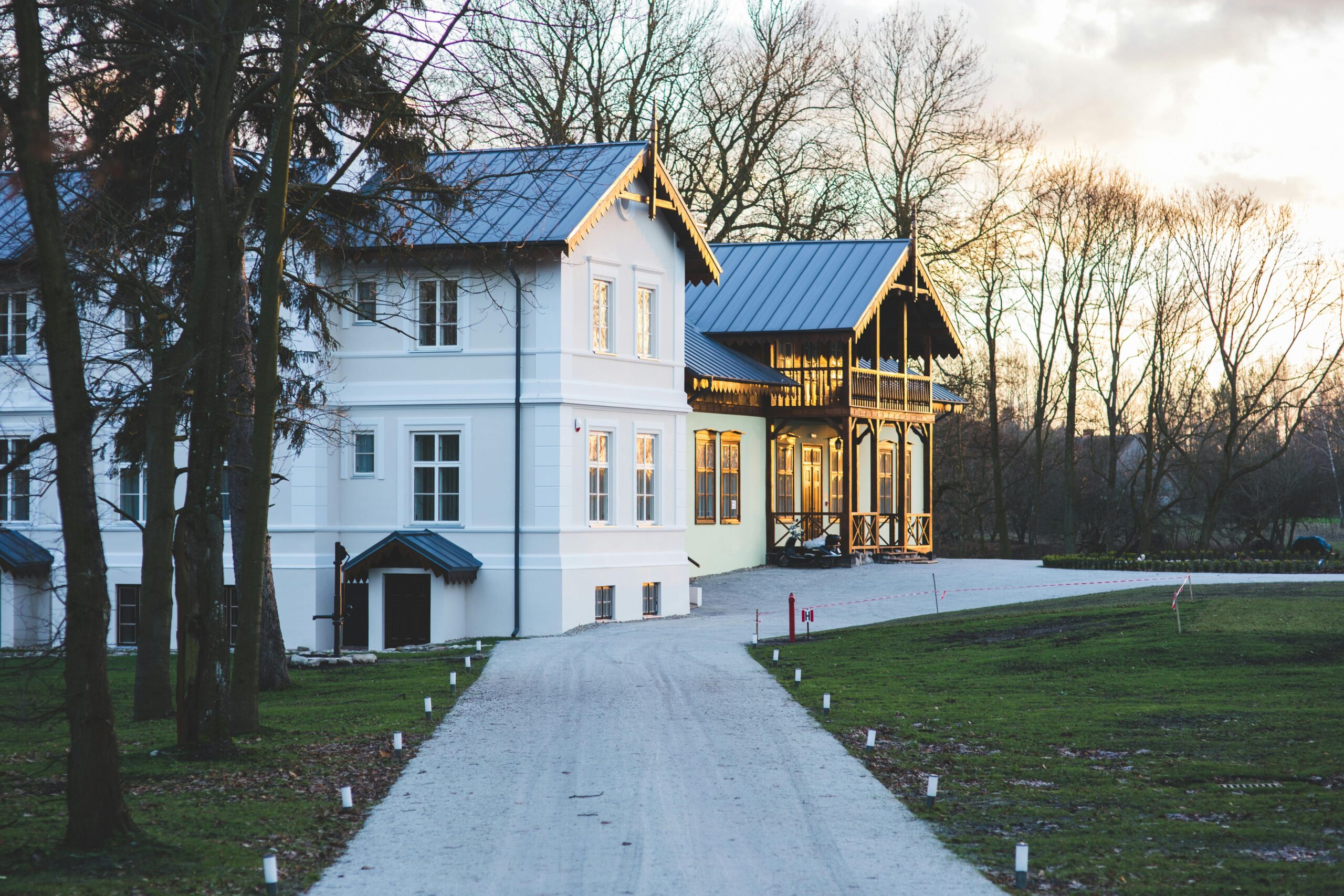 White mansion with a garden and driveway at sunset, showcasing elegant architecture.
